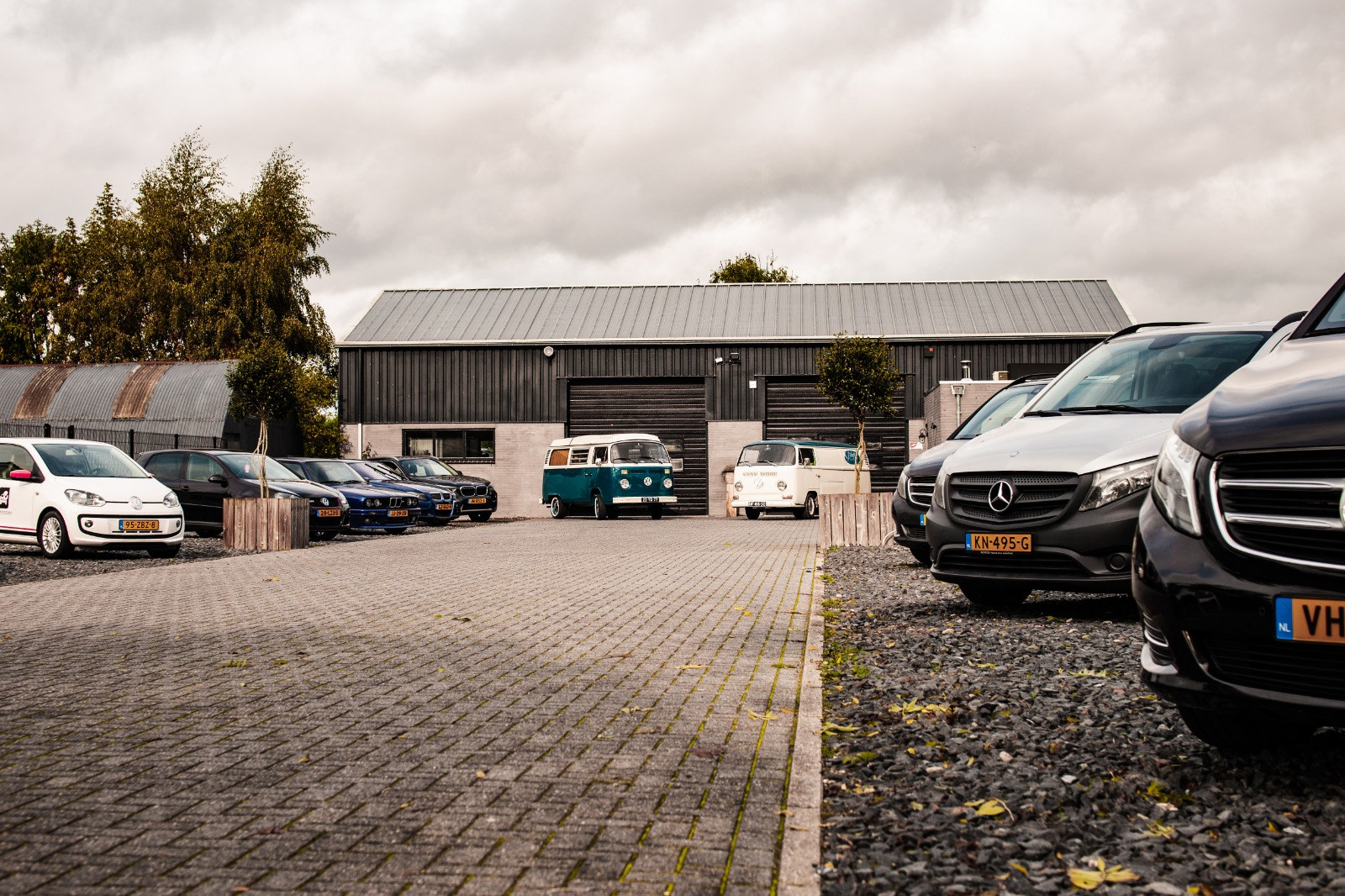 Het pand met de donkere gevel, een VW T2-busje en bedrijfswagens op het terrein